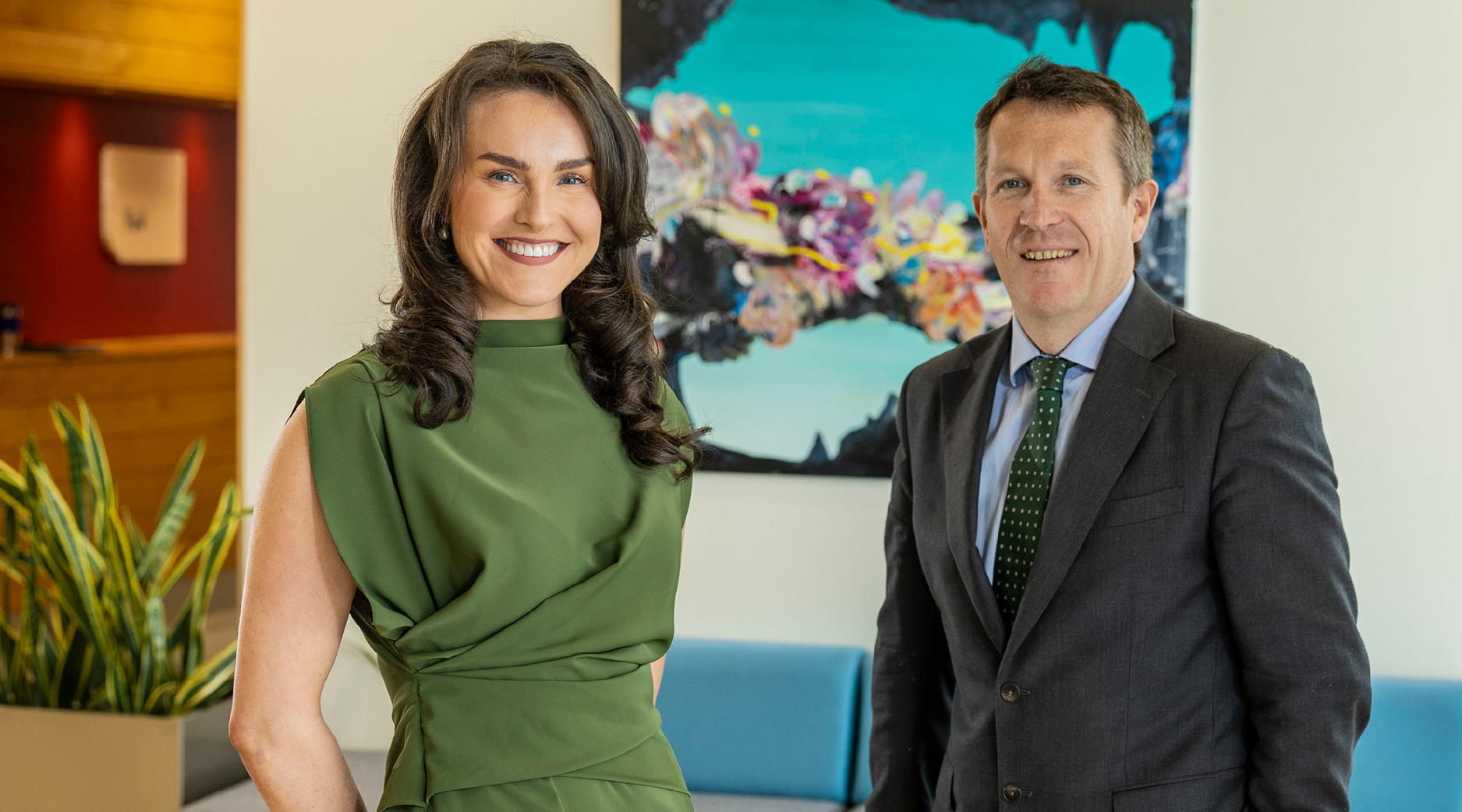 A smiling woman in a green dress with a man in a grey suit, blue shirt and green tie